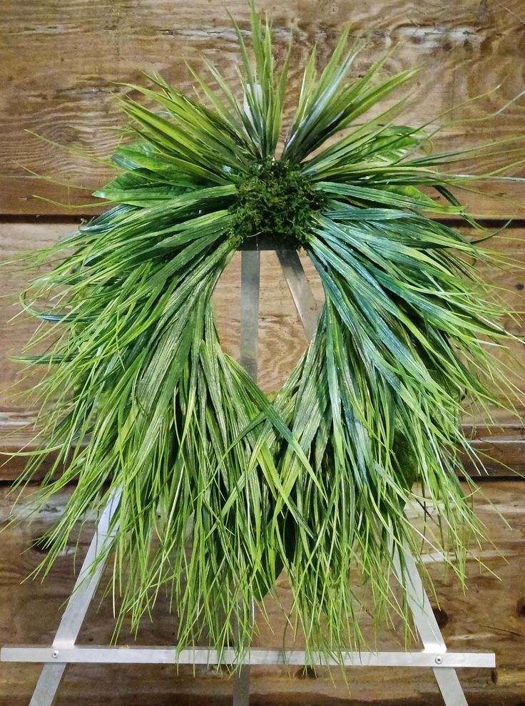 a green wreath is hanging on the side of a wooden wall with grass in it