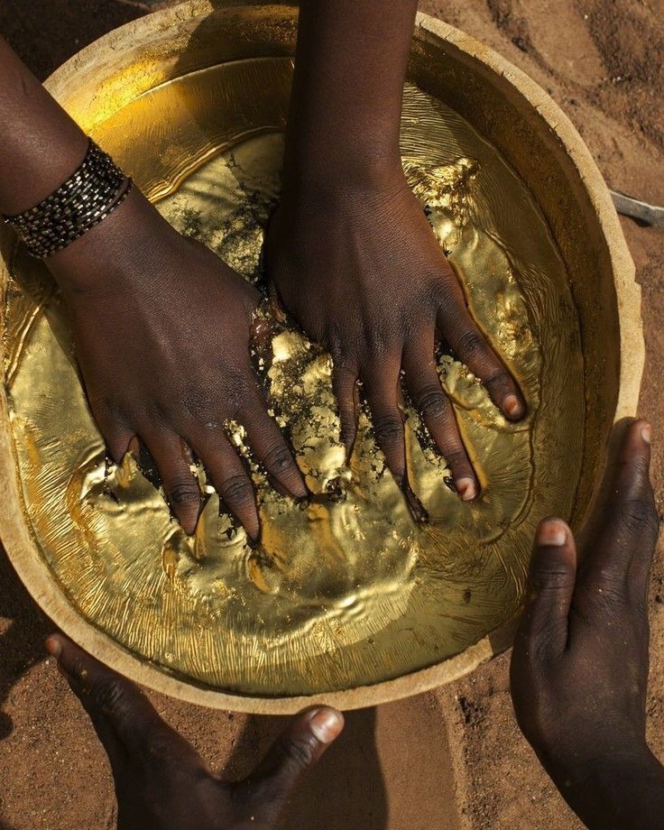 two hands reaching into a bowl with gold flakes on the bottom and one hand in it