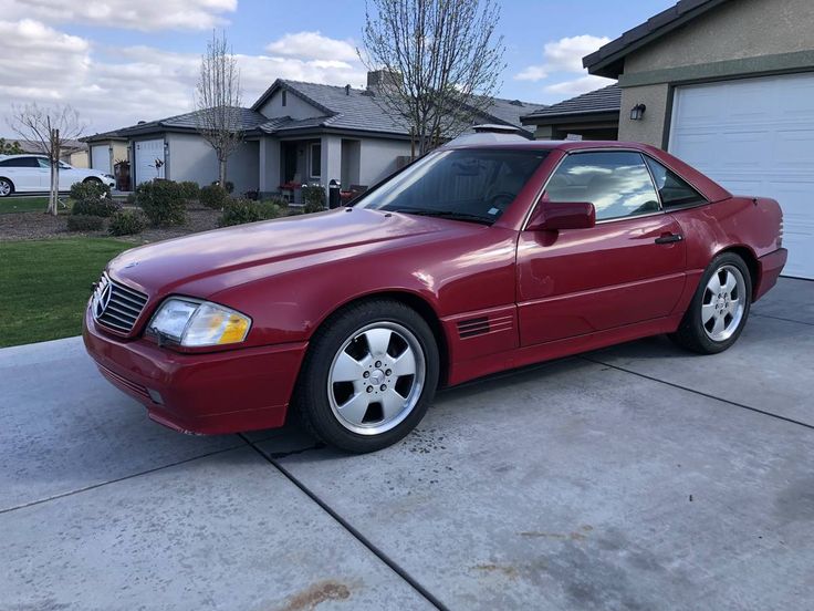 a red mercedes benz coupe parked in front of a house with two garage doors open