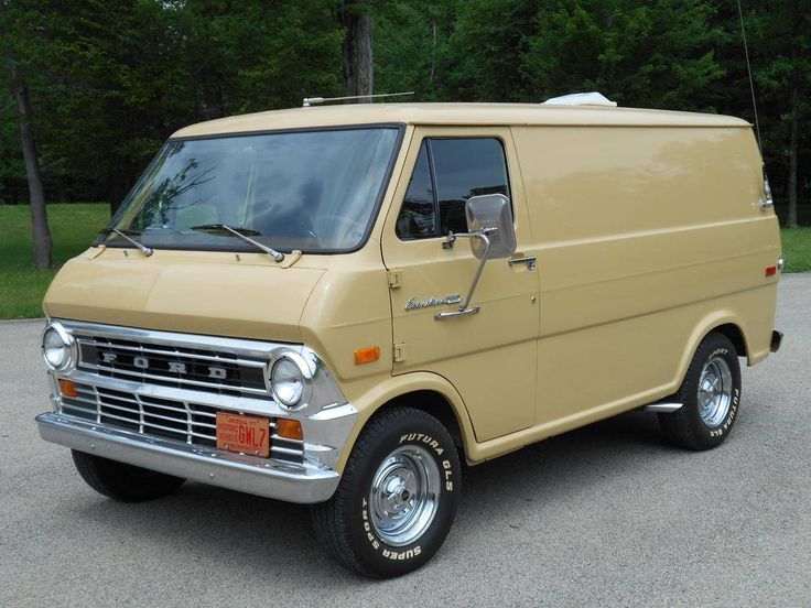 an old yellow van parked in a parking lot with trees in the backgroud