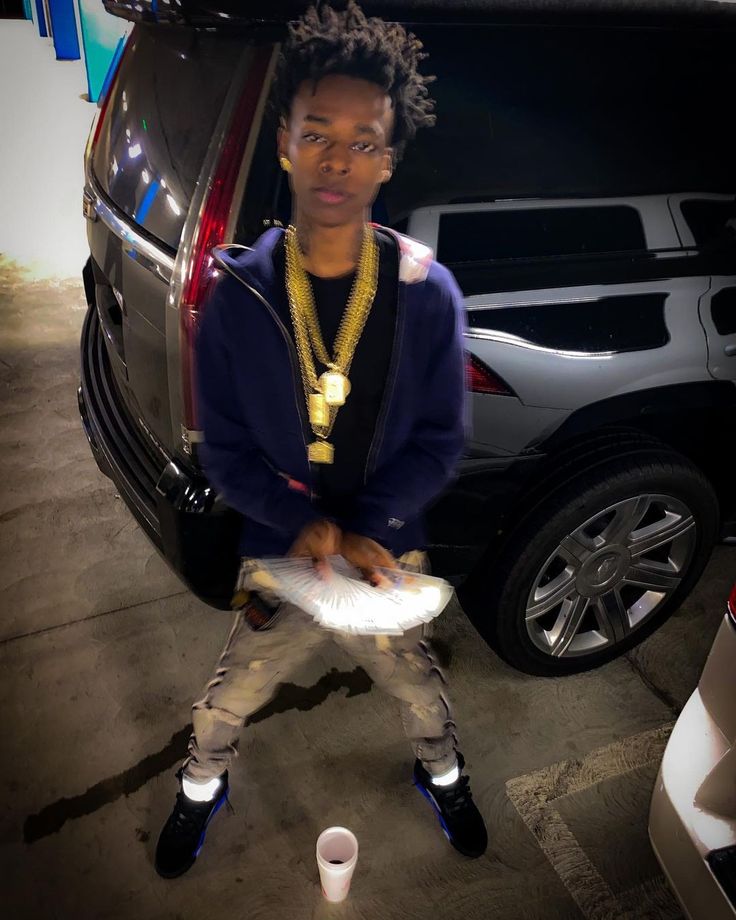 a young man holding a frisbee in front of a parked car at night