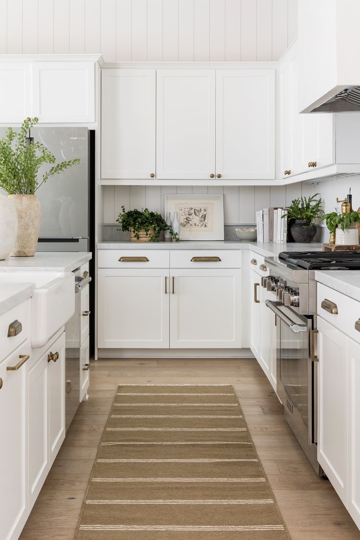 a kitchen with white cabinets and beige rug on the floor in front of the stove