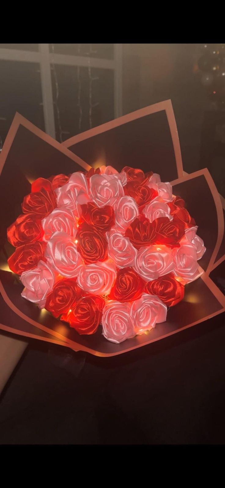 a bunch of red roses sitting on top of a glass bowl filled with light up petals