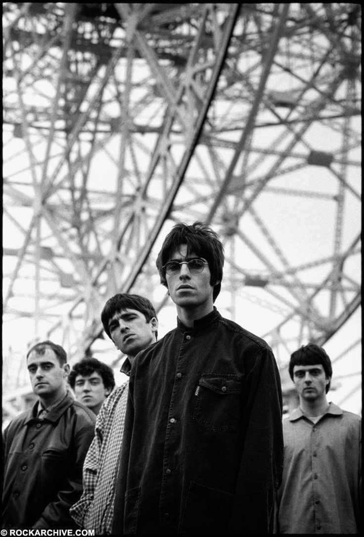 black and white photograph of young men standing in front of an electrical tower with one man looking at the camera