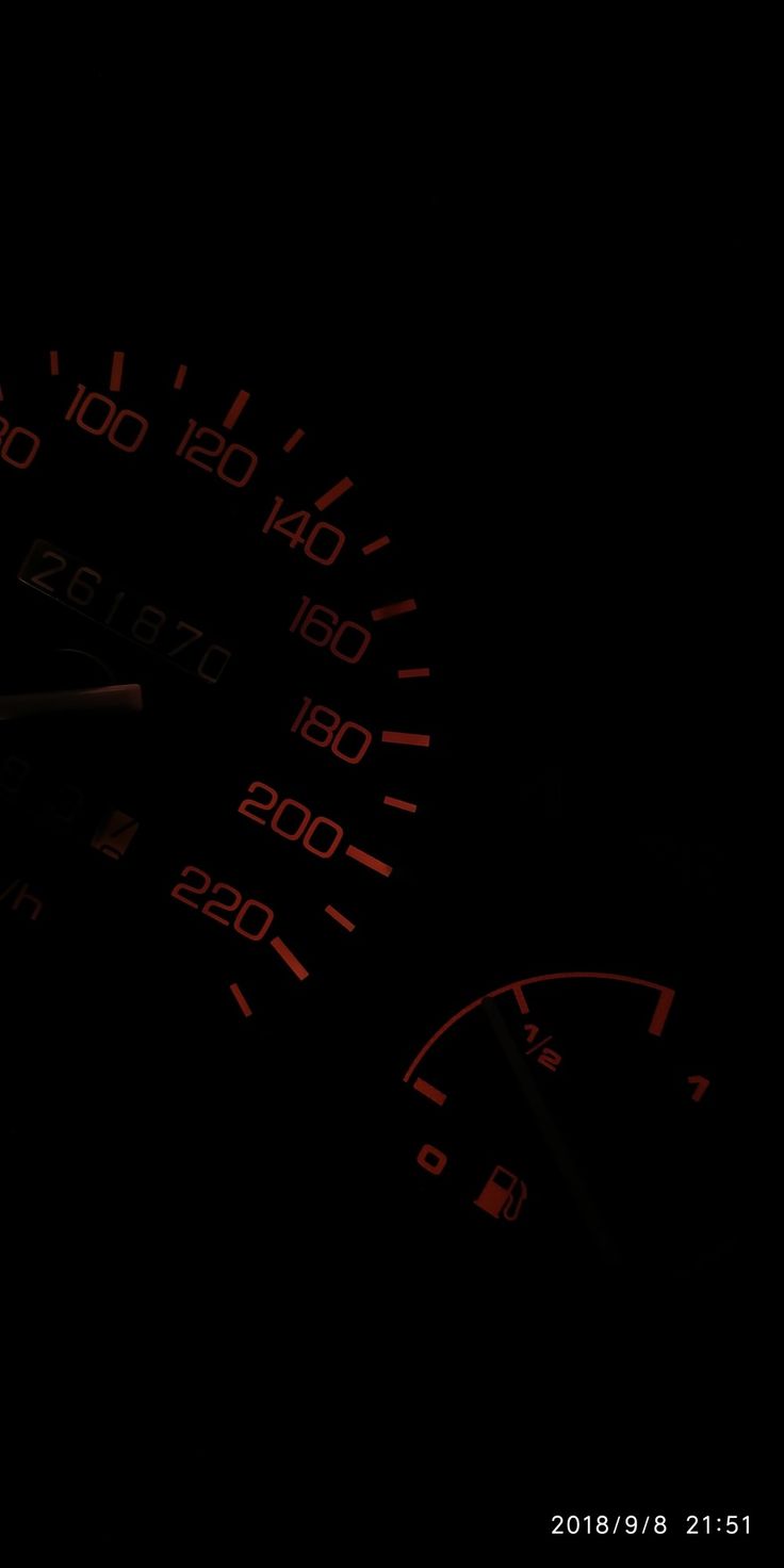 the speedometer is lit up in the dark with red numbers on it's face