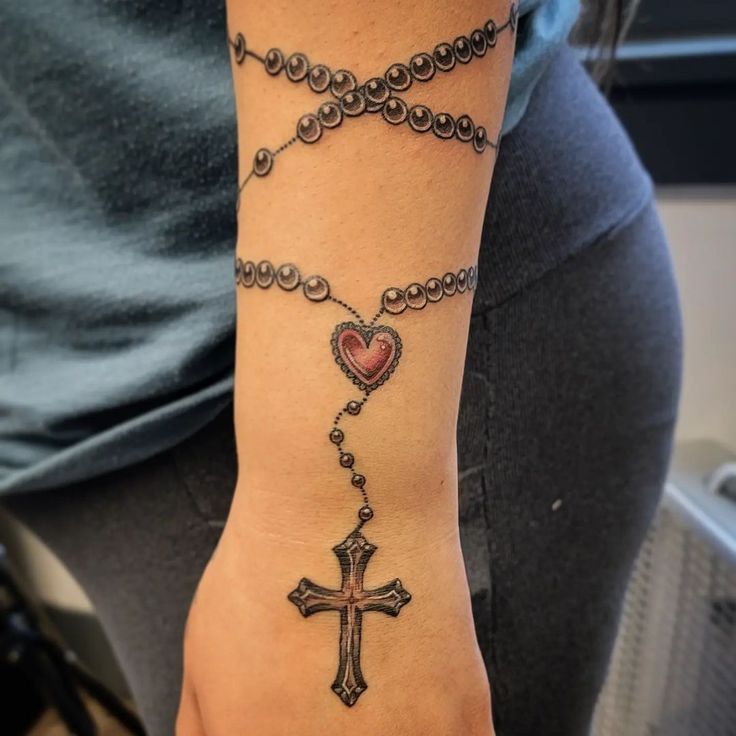 a woman's arm with a rosary and heart tattoo on the wrist that is attached to a cross