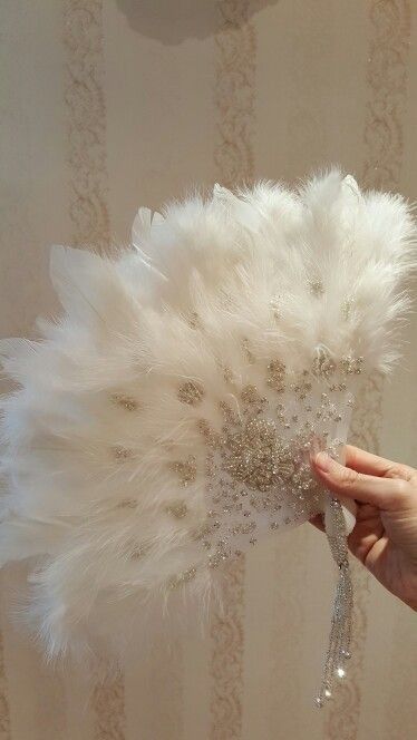 a white feather fan is being held by a woman's hand in front of a wall