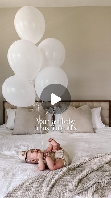 a baby laying on top of a bed next to white balloons