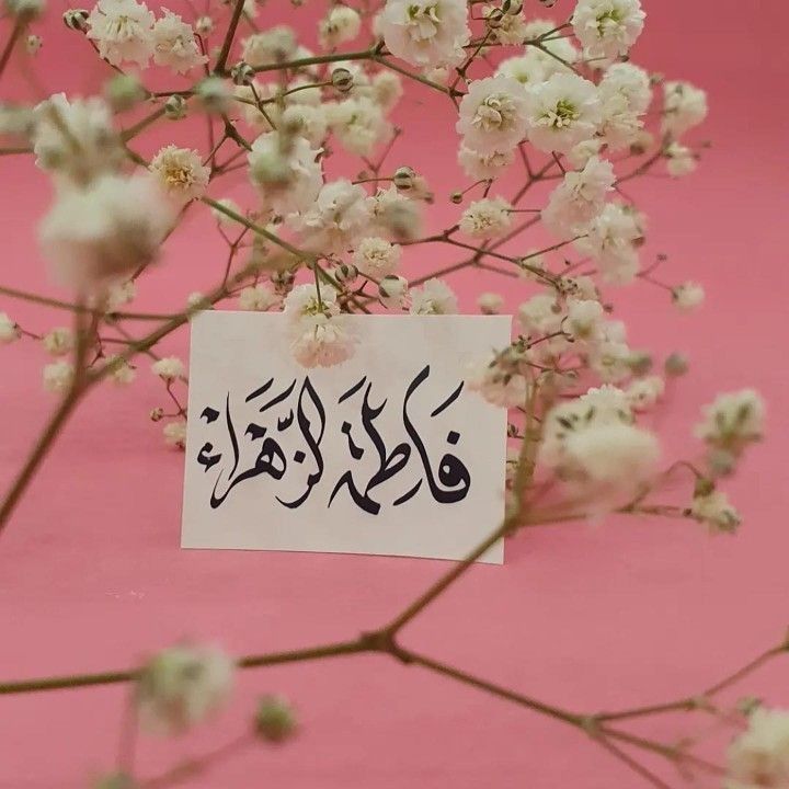 a piece of paper with arabic writing on it sitting next to some white and pink flowers