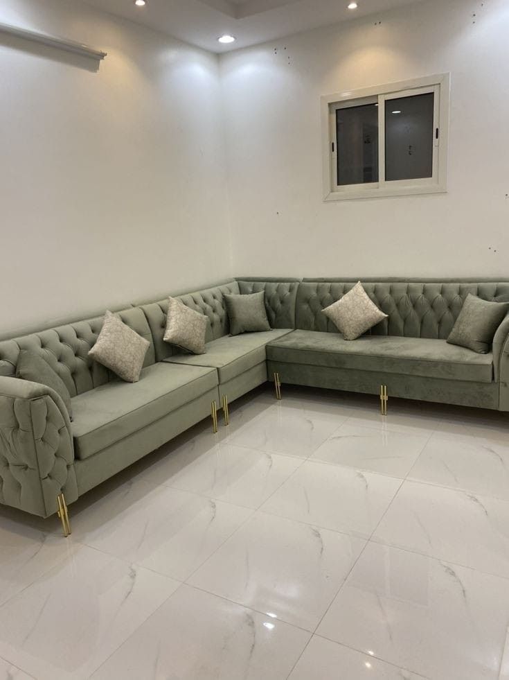 a large sectional couch in a room with white tile flooring and walls, along with two windows