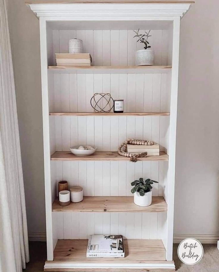 a white bookcase with wooden shelves and plants