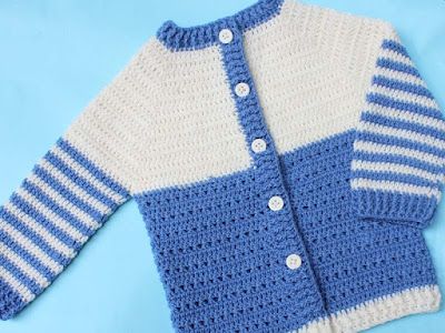 a blue and white crocheted sweater is laying on a blue surface with buttons