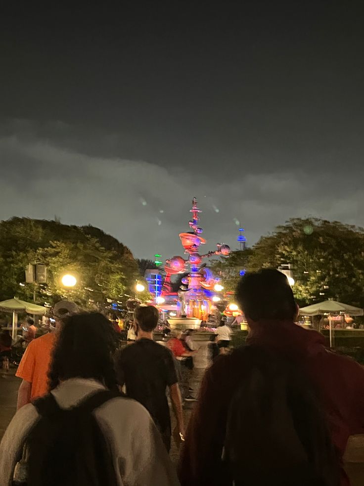 people walking down the street at night with fireworks in the sky and buildings lit up behind them