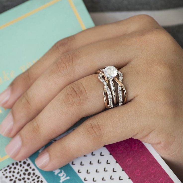 a woman's hand with a ring on top of her finger and a book in the background