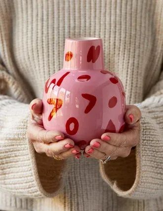 a woman holding a pink vase with red numbers on the front and bottom, in her hands