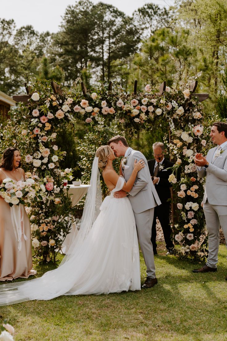 a bride and groom kissing in front of an outdoor ceremony arch with flowers on it