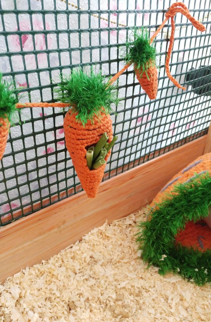 some carrots are hanging on the side of a wire mesh fence with grass growing out of them