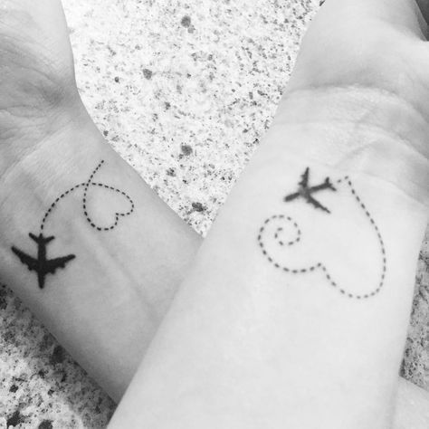 two people holding hands with small tattoos on their wrist and one has an airplane in the sky