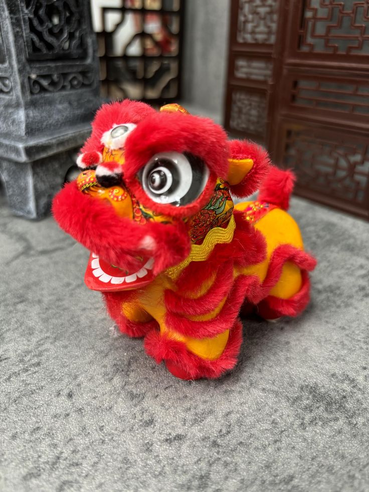 a red and yellow stuffed animal sitting on top of a cement floor next to a fire hydrant