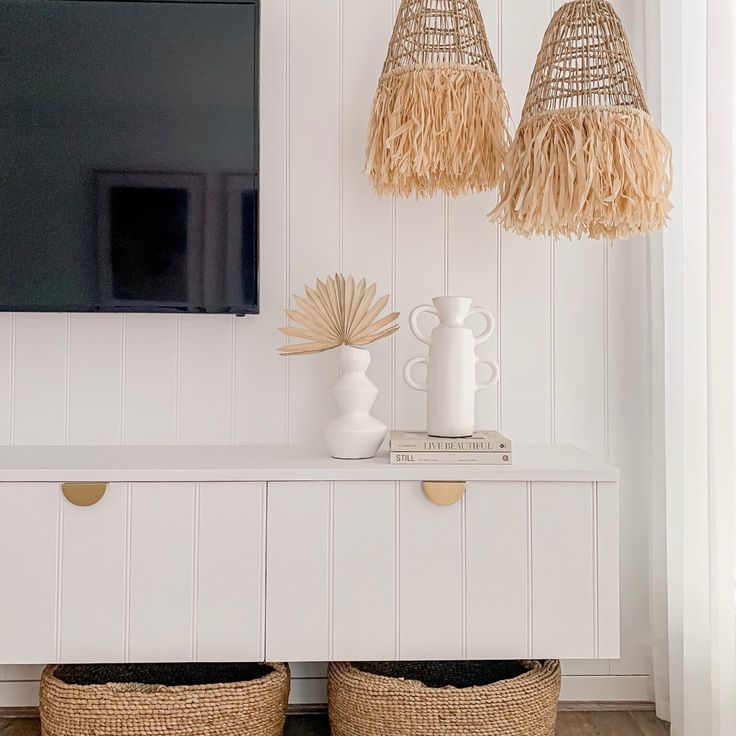 two wicker baskets sit on top of a white cabinet in front of a flat screen tv