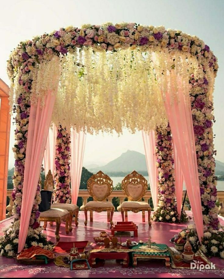 an outdoor wedding setup with pink drapes and white flowers on the ceiling, along with chairs