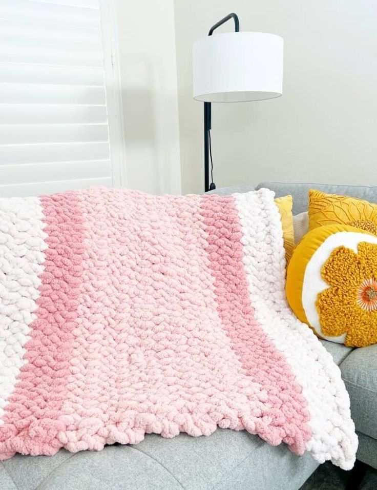 a pink and white crocheted blanket sitting on top of a couch next to a yellow pillow