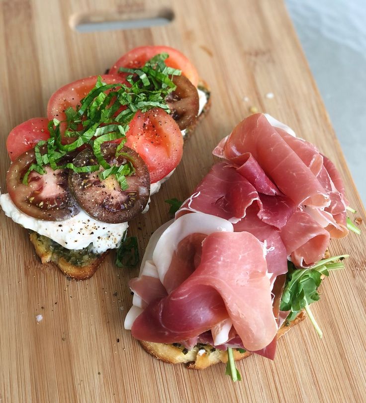 a wooden cutting board topped with two open faced sandwiches covered in meat and veggies