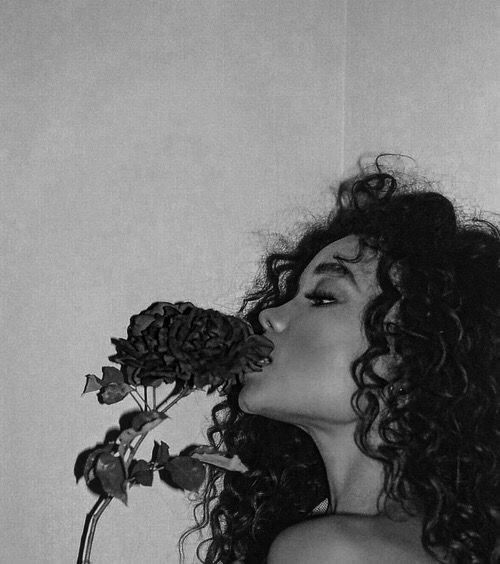 a black and white photo of a woman smelling a flower