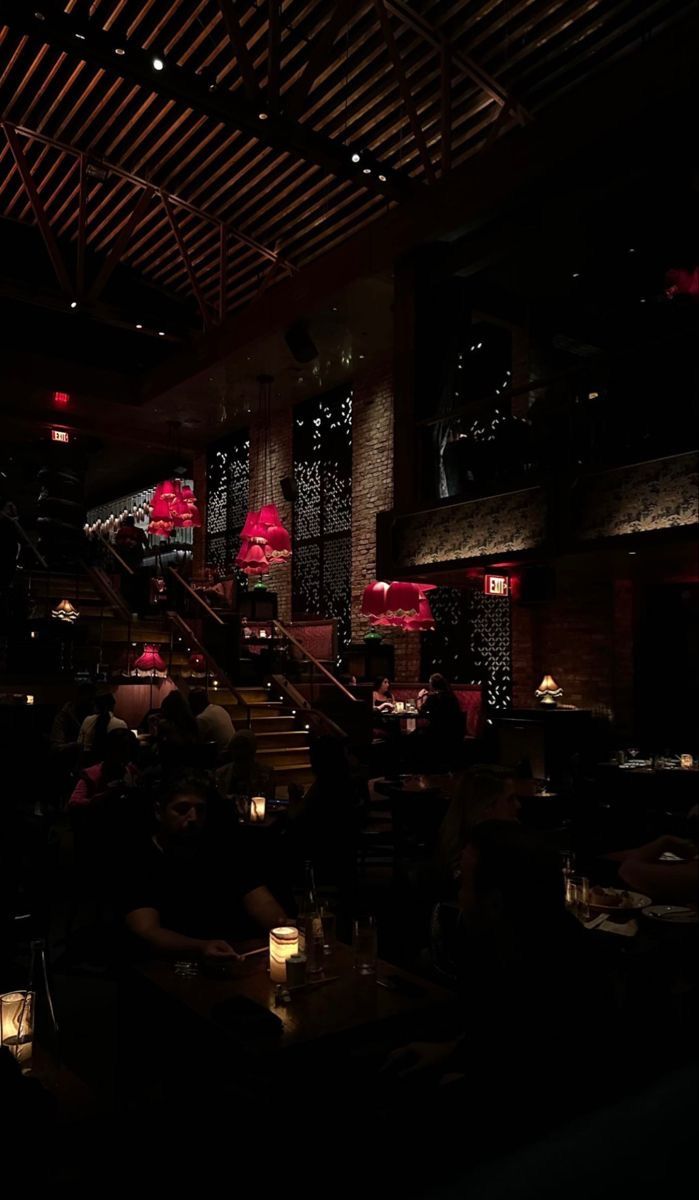 people sitting at tables in a dimly lit restaurant with red lights on the walls and ceiling