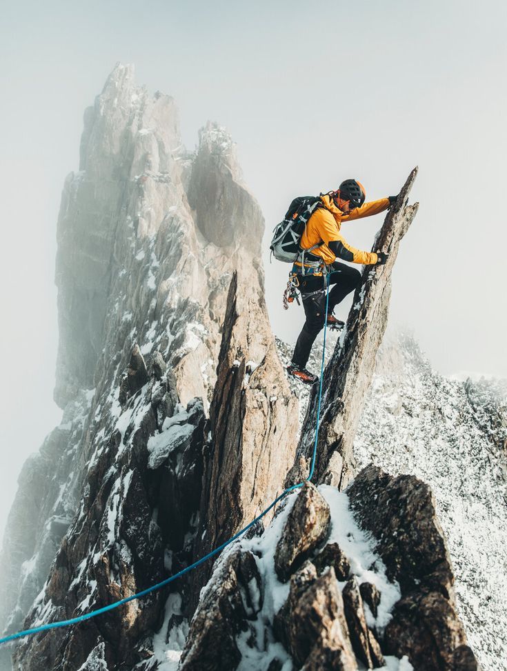 a man climbing up the side of a snow covered mountain with a rope attached to it