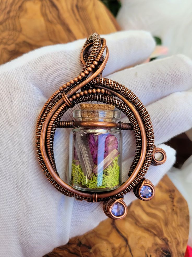 a hand holding a glass jar filled with different colored stones and wire wrapped around it