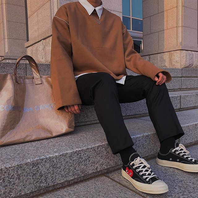 a man sitting on the steps with his feet crossed and wearing black pants, a brown sweater and white sneakers