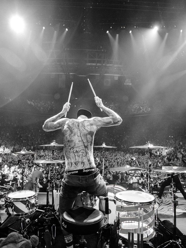 a man with tattoos on his back playing drums in front of an audience at a concert