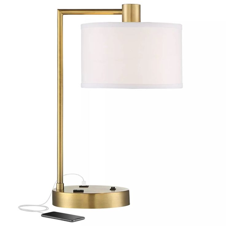 a table lamp with a phone plugged in to the side and a white shade on top