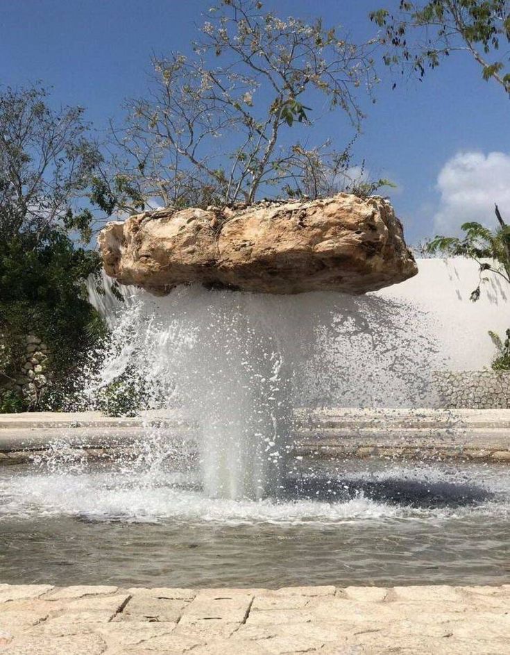 a large rock sticking out of the top of a water fountain in front of trees