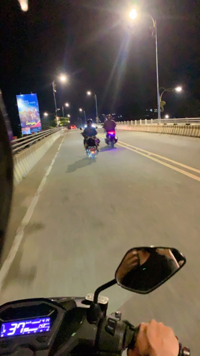 two people riding motorcycles on a highway at night