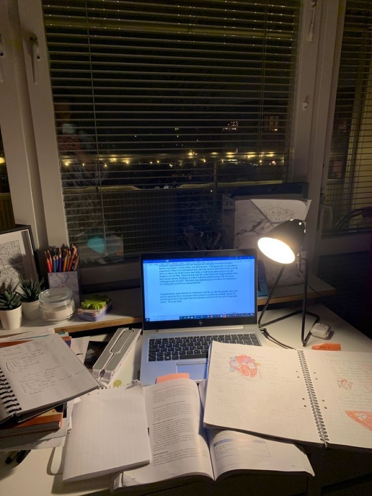 an open laptop computer sitting on top of a desk next to a lamp and books