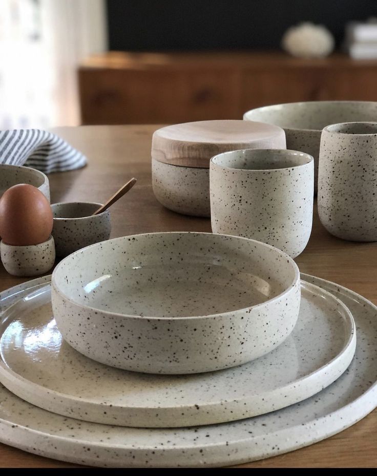 a table topped with white dishes and plates covered in speckled glazes on top of a wooden table