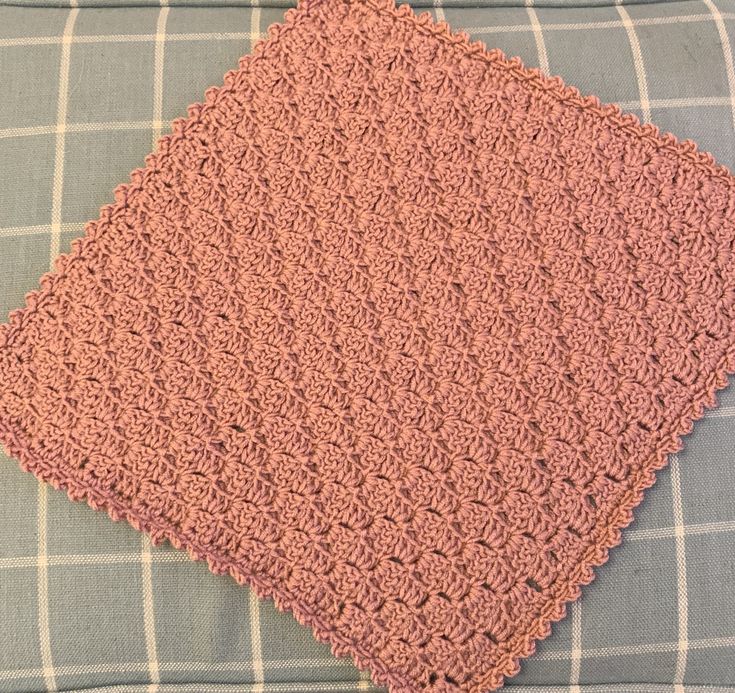 a pink crocheted blanket sitting on top of a blue and white checkered pillow