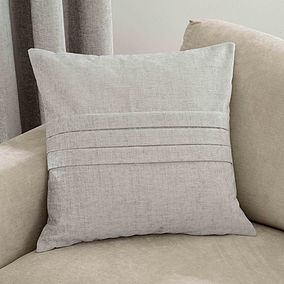 a white pillow sitting on top of a beige couch next to a window with drapes