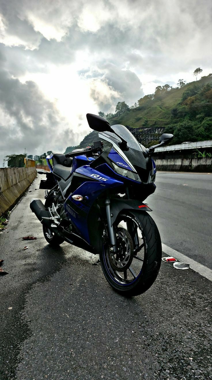 a blue motorcycle parked on the side of a road next to a fence and trees