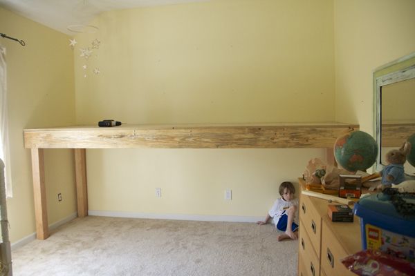 a young child sitting on the floor in front of a wooden desk and shelf above it