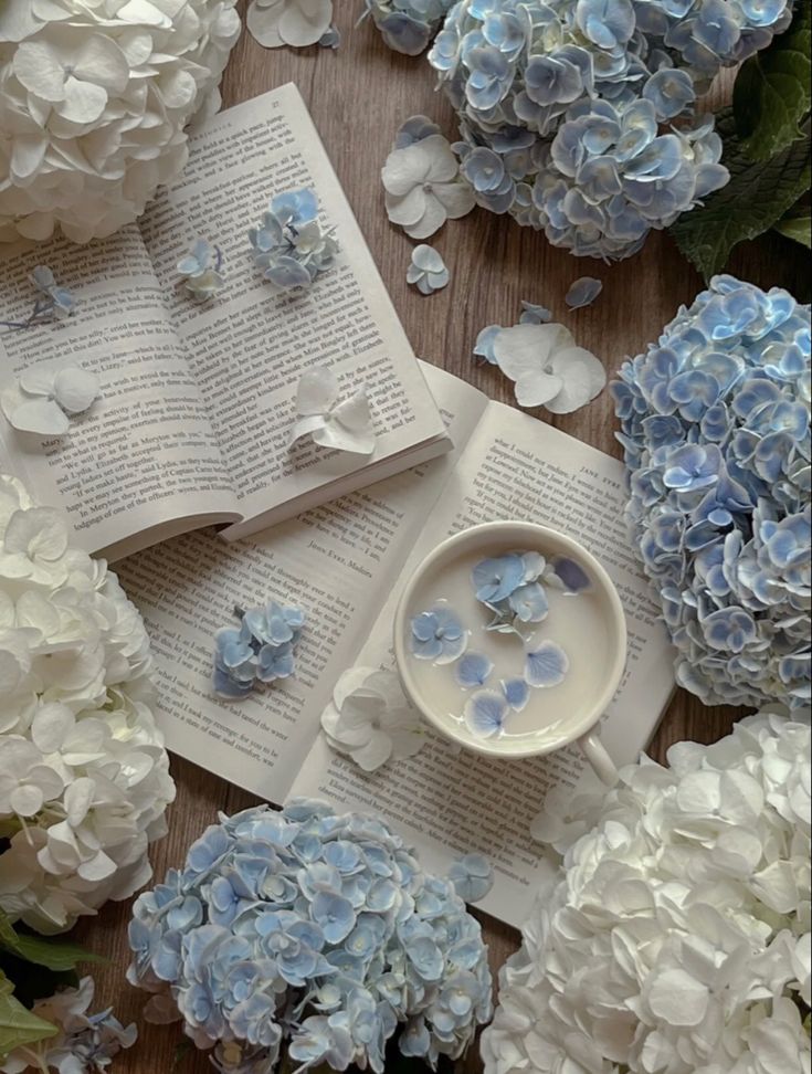 blue and white hydrangeas are scattered around an open book