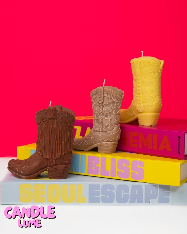 two candles are sitting on top of some books with cowboy boots next to each other