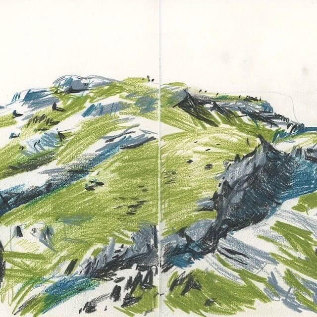 an open book with some colored pencils on top of it and a mountain in the background