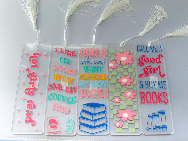 three bookmarks with flowers and books on them are hanging from the side of a table