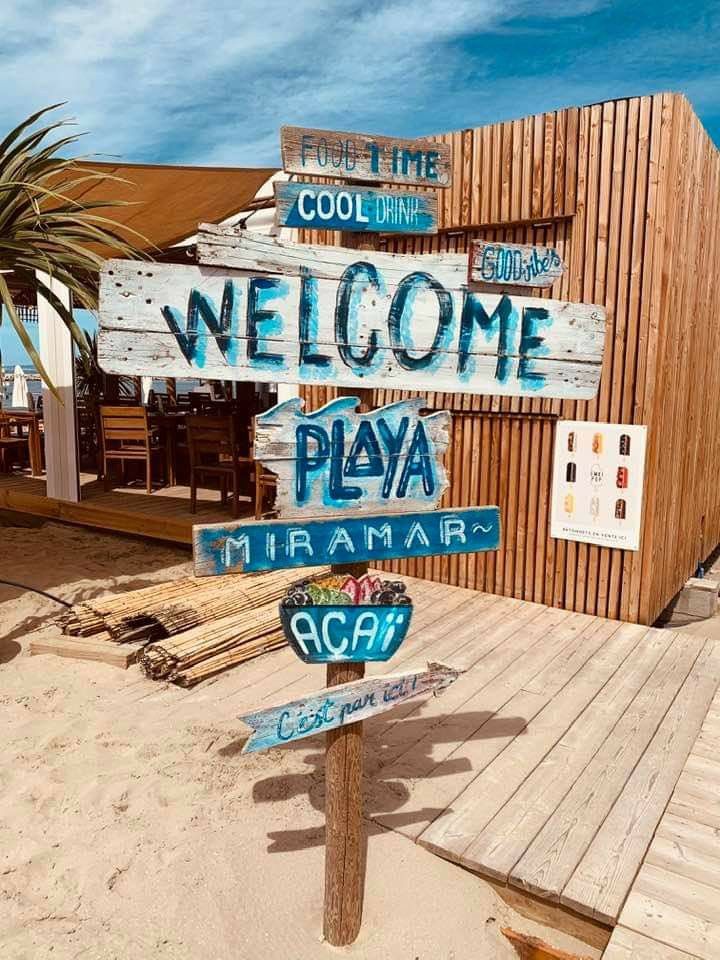 a wooden sign that says welcome to playa maramar and the ocean in front of a building