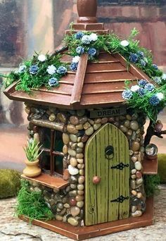 a small house made out of rocks and stones with blue flowers on the roof is shown