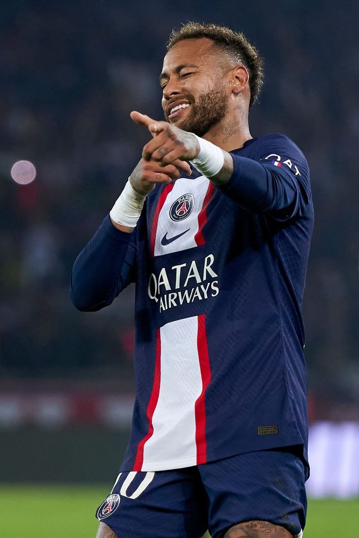 a soccer player is smiling and pointing to the sidelines with his hands in the air