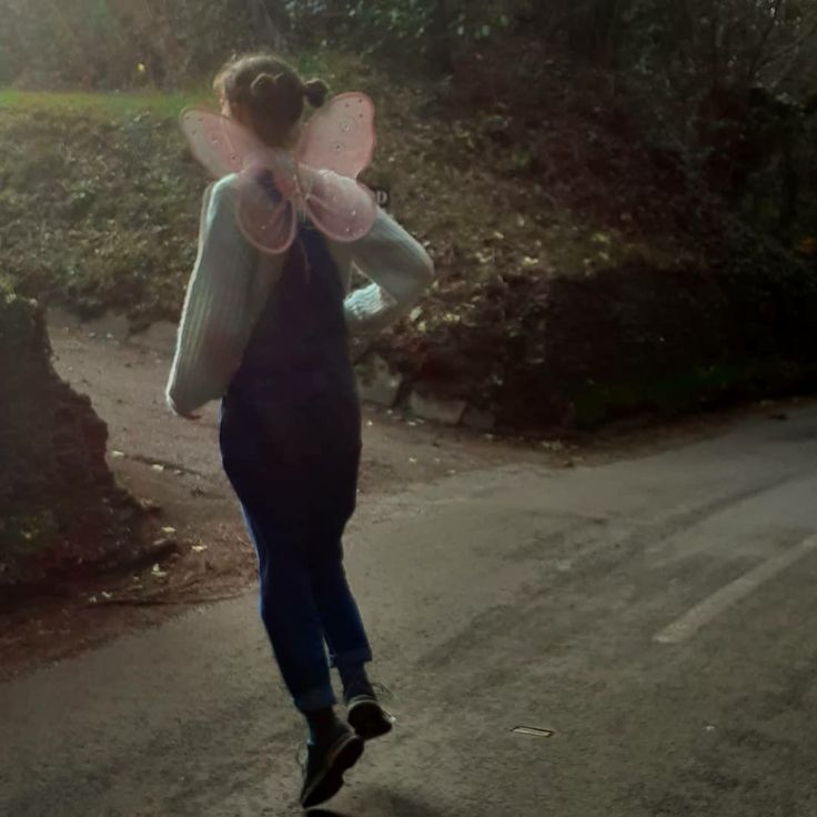 a woman walking down a road with a pink fairy wings on her head and back